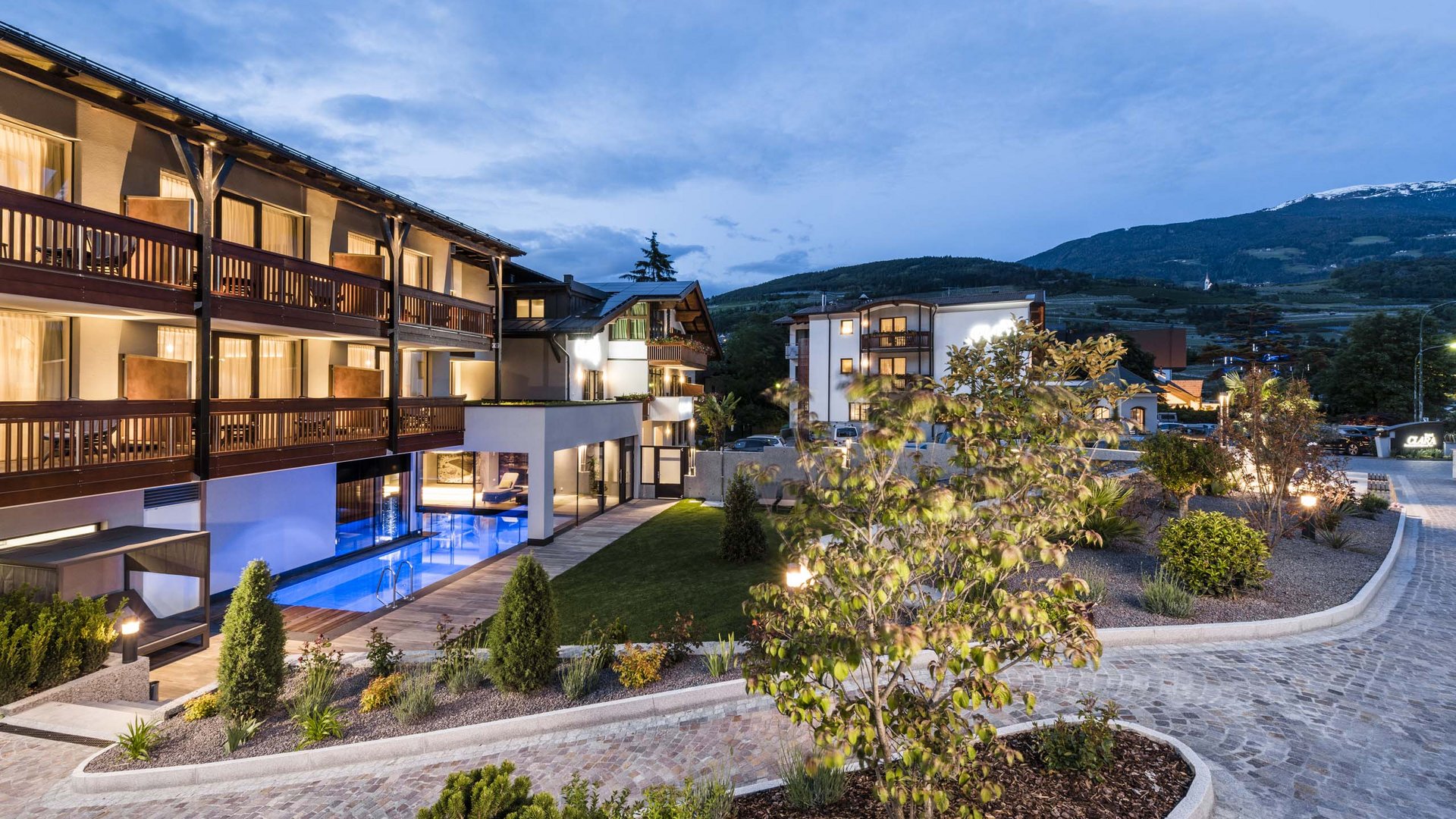Abendaufnahme eines modernen Hotels mit beleuchtetem Pool und Bergblick